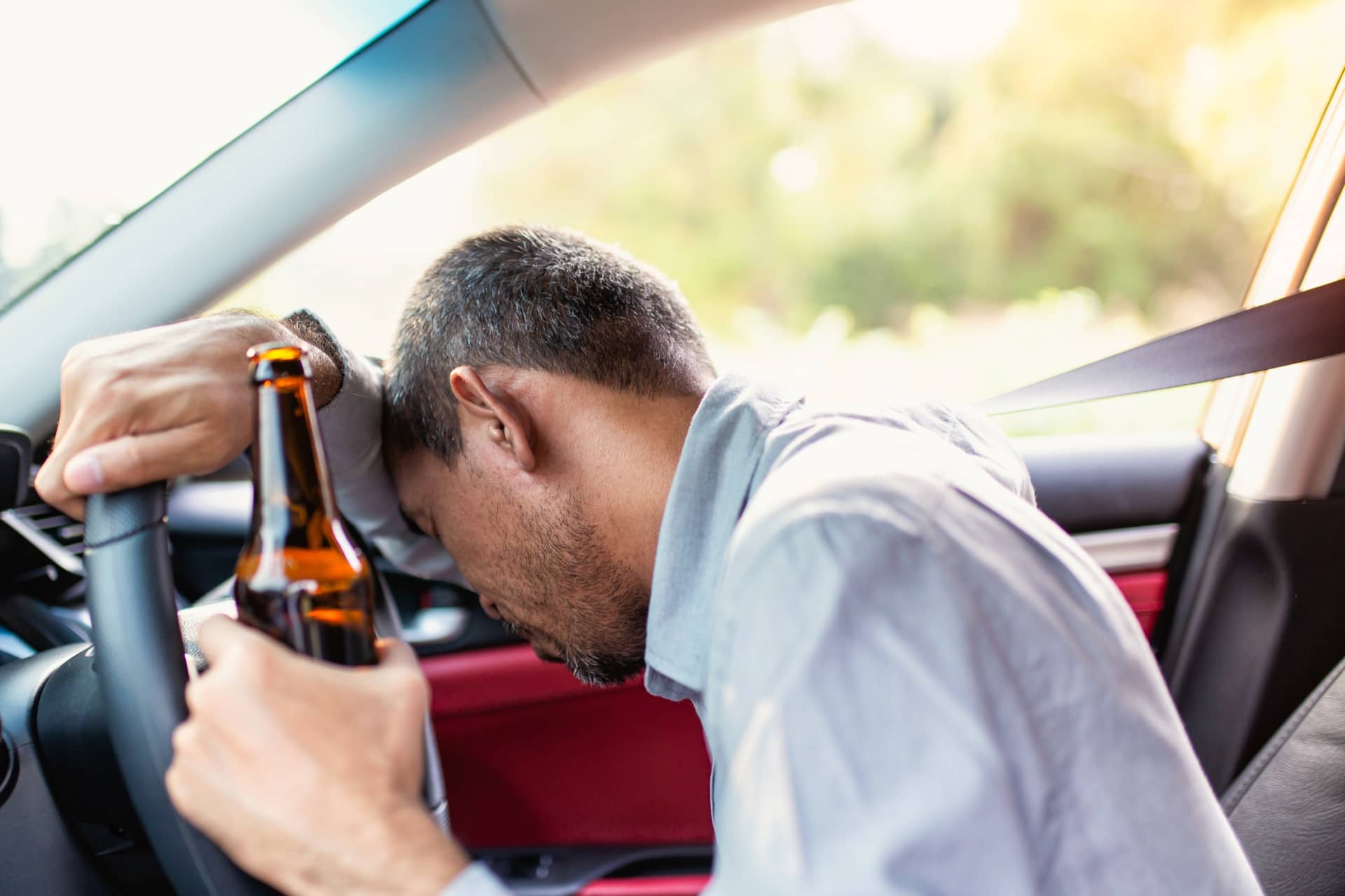 Persona en un carro con bebida en la mano pensando en contratar a un abogado de accidentes por DUI